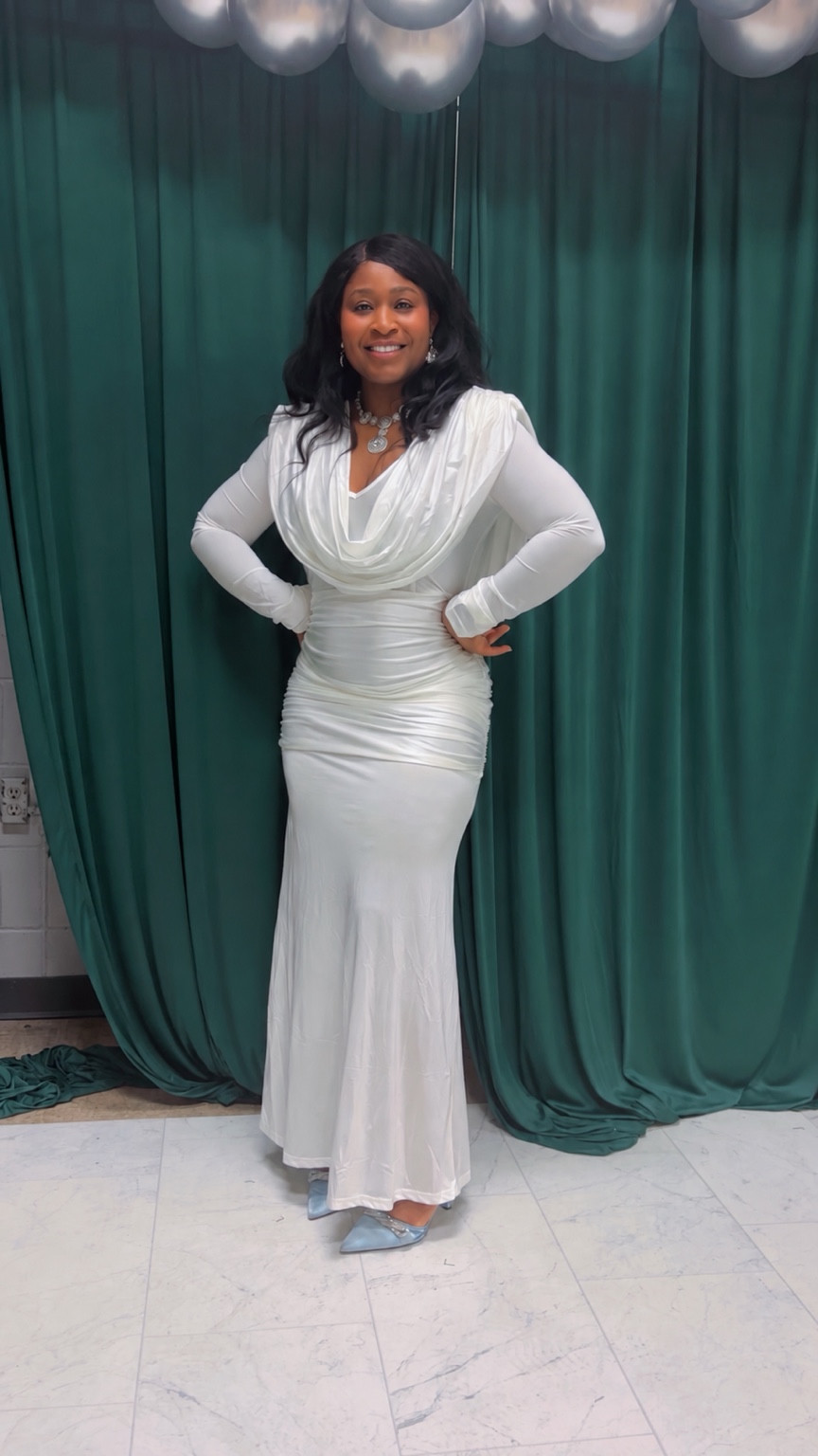 Jojo Sulaimon smiling in a white dress against green curtains